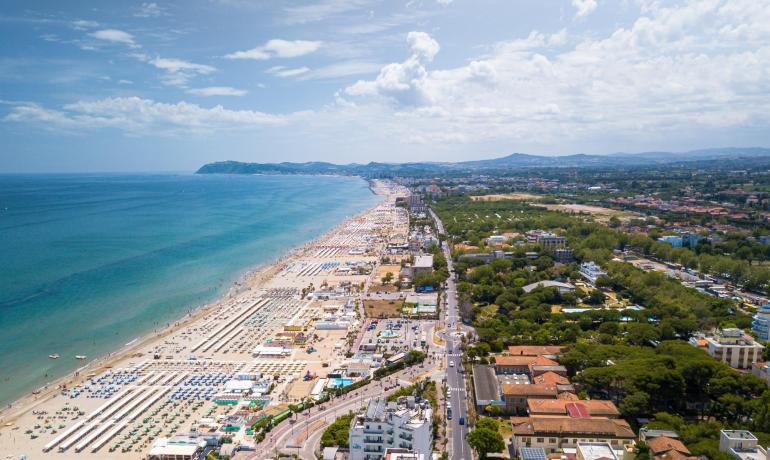 Spiaggia affollata con ombrelloni e mare azzurro, vista dall'alto.