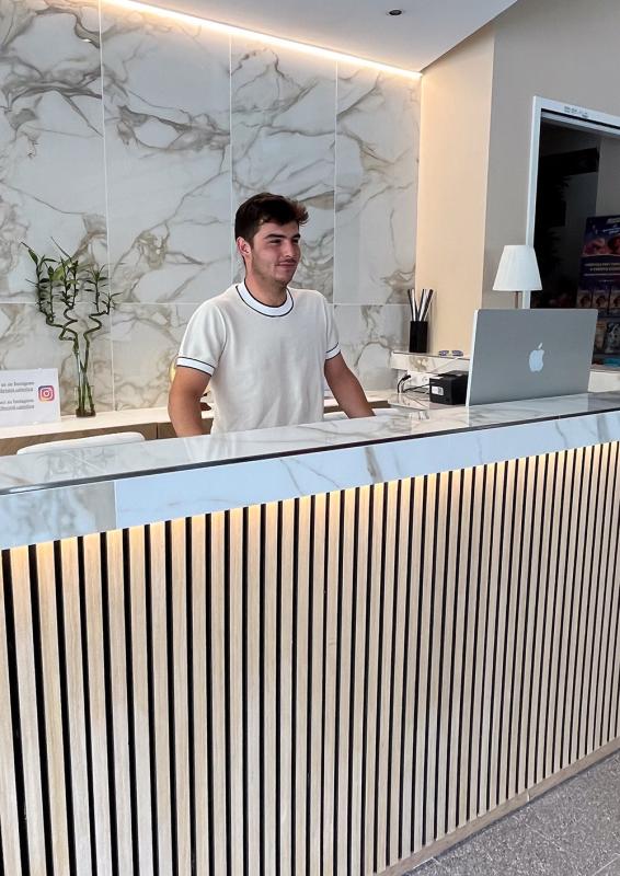 Receptionist standing behind a modern desk with a laptop.